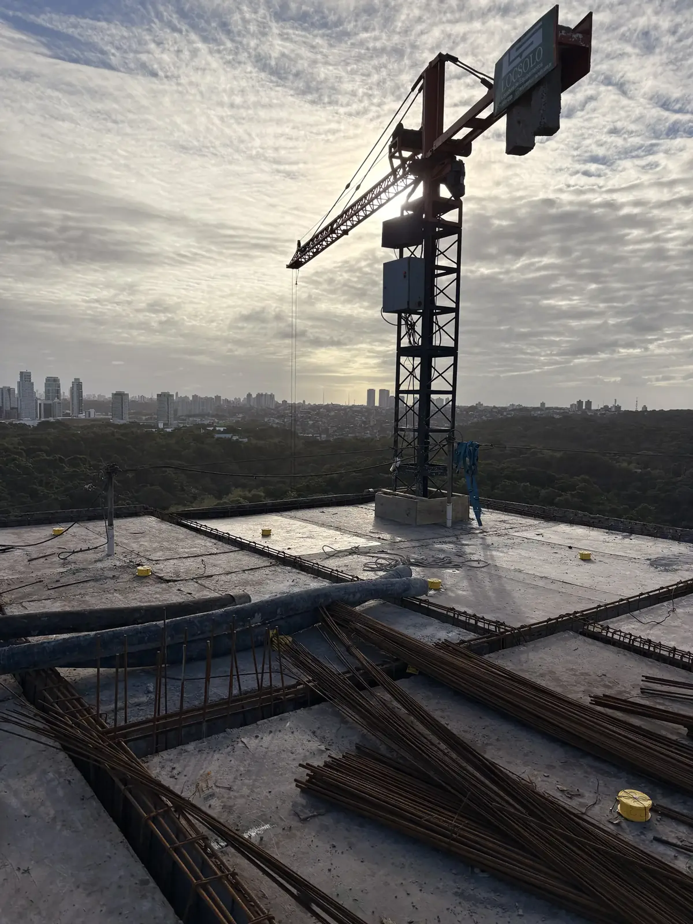 Guindaste de torre em canteiro de obras da Pilares ao fim da tarde, com a cidade ao fundo